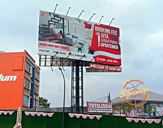 Billboard besar dengan tulisan dan logo di sisi jalan raya